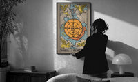 Wheel of Fortune print in a slim black frame being hung on a sunlit wall in a monochrome room