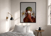 White Flowers Over the Face print in a black frame above a bed with striped linens, a brass wall lamp and a sunlit window