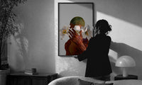 White Flowers Over the Face print in a slim black frame being hung on a sunlit wall in a monochrome room
