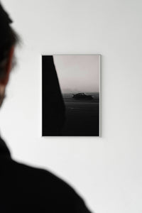 White-framed Porsche 911 print on a white wall with a silhouetted person standing in the foreground