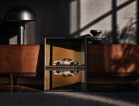 Black-framed White 911 Hangar Sunset Reflection print on the floor in front of a dark wooden console