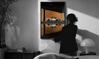 White 911 Hangar Sunset Reflection print in a slim black frame being hung on a sunlit wall in a monochrome room