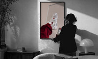 White Sneakers with Burgundy Trousers print in a slim black frame being hung on a sunlit wall in a monochrome room