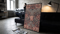Ornate floral honeysuckle pattern print in a slim black frame leaning on a dark sofa in a concrete print studio