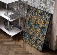 Ornate floral vine pattern poster in a black frame leaning beside a shelf in a raw-plaster loft