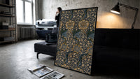 Ornate floral vine pattern print in a slim black frame leaning on a dark sofa in a concrete print studio