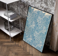 Floral marigold pattern with leaves poster in a black frame leaning beside a shelf in a raw-plaster loft