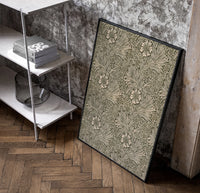 Floral marigold vine pattern poster in a black frame leaning beside a shelf in a raw-plaster loft