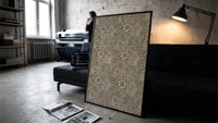 Floral marigold vine pattern print in a slim black frame leaning on a dark sofa in a concrete print studio