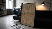 Floral bird damask textile pattern print in a slim black frame leaning on a dark sofa in a concrete print studio