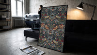 Birds and strawberries floral pattern print in a slim black frame leaning on a dark sofa in a concrete print studio