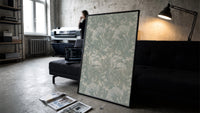 Ornate floral tulip leaf pattern print in a slim black frame leaning on a dark sofa in a concrete print studio