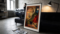 Witch with broom peering through window print in a slim black frame leaning on a dark sofa in a concrete print studio
