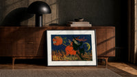 Witch flying on broomstick with pumpkin print in a black frame leaning against a walnut console in lamplight