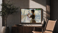 Woman hanging laundry outdoors print in a wood frame above a fluted sideboard beside an olive tree