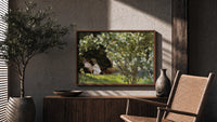 Woman reading in garden chair print in a wood frame above a fluted sideboard beside an olive tree