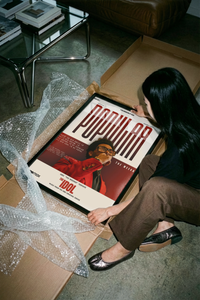 Woman unwrapping The Weeknd Popular Idol poster from a cardboard box lined with bubble wrap
