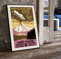 Erupting volcano over lake print in a black frame leaning beside a vintage door on parquet