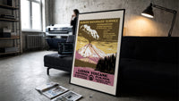 Erupting volcano over lake print in a slim black frame leaning on a dark sofa in a concrete print studio