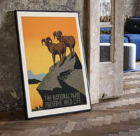 Two bighorn sheep on rocky cliff print in a black frame leaning beside a vintage door on parquet