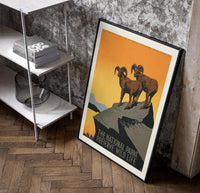 Two bighorn sheep on rocky cliff poster in a black frame leaning beside a shelf in a raw-plaster loft