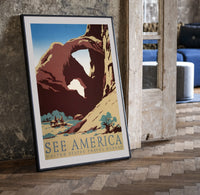 Desert rock arch with riders print in a black frame leaning beside a vintage door on parquet