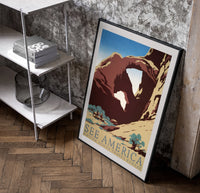 Desert rock arch with riders poster in a black frame leaning beside a shelf in a raw-plaster loft