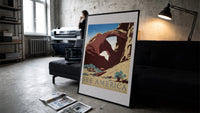 Desert rock arch with riders print in a slim black frame leaning on a dark sofa in a concrete print studio