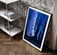 Cave stalactites with two tourists poster in a black frame leaning beside a shelf in a raw-plaster loft