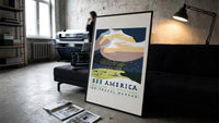 Snowy mountain with Native American camp print in a slim black frame leaning on a dark sofa in a concrete print studio